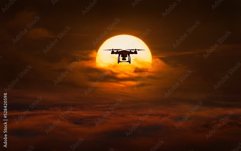 Silhouette of flying quadcopter against background of glowing sun Silhouette of flying quadcopter against background of glowing sun
