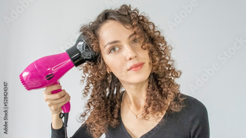 Woman gives herself a curly hairstyle. Hair care concept. A curly woman dries her hair at home with a hair dryer with a diffuser attachment. A beautiful girl uses a modern hair dryer. photo