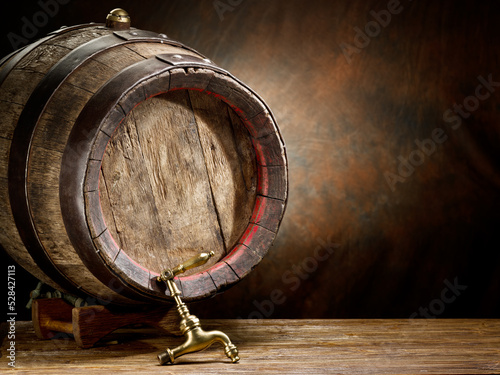 Wooden wine or beer barrel with metal hoops on the wooden table at the brown background.