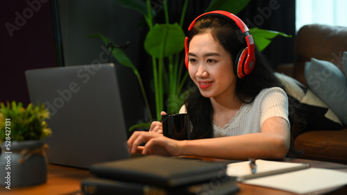 Pretty young lady wearing headphone, listening lecture during study online on laptop. Education, e-learning, distance training