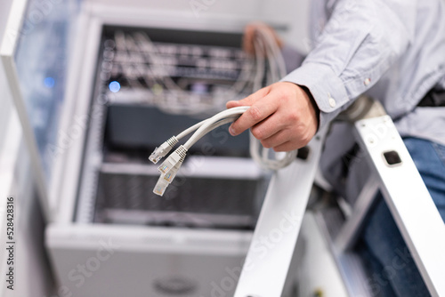 Male worker configures local network by holding cables and plugs to connect to server.
