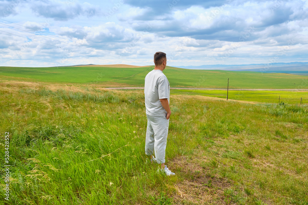 A man in light-colored clothes stands on the cliff of a hill and looks towards the Buryat Selenga River near the city of Ulan-Ude A man in light-colored clothes stands on the cliff of a hill and looks towards the Buryat Selenga River near the city of Ulan-Ude