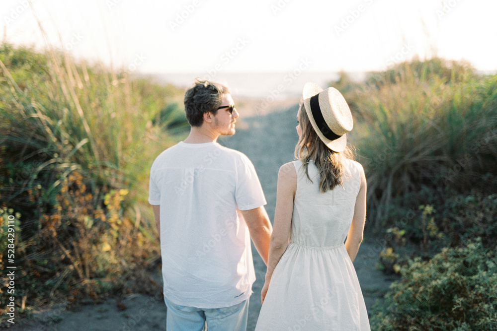 Woman in a straw hat stands next to a man on a country road. Back view