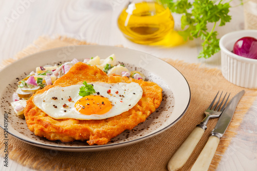 Viennese pork schnitzel with a fried egg. Served on potato salad. Natural wooden planks in the background. photo