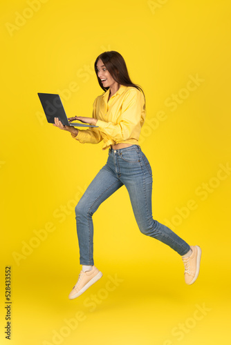 Excited Lady Using Laptop Running Posing Over Yellow Background, Vertical