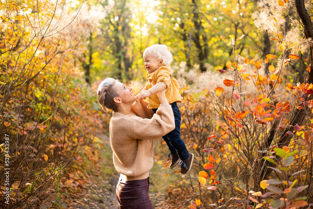 Happy young mother playing with her little baby son on sunshine warm autumn