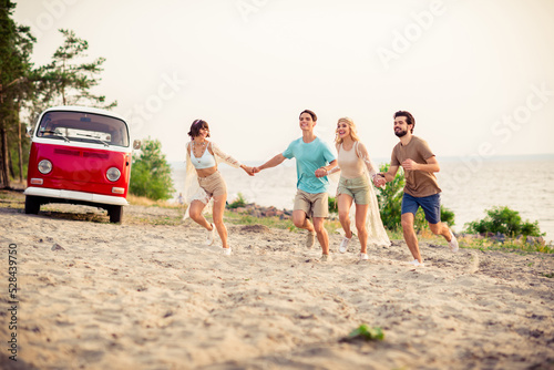 Photo of charming adorable hippie people company smiling running together holding arms outside seaside beach