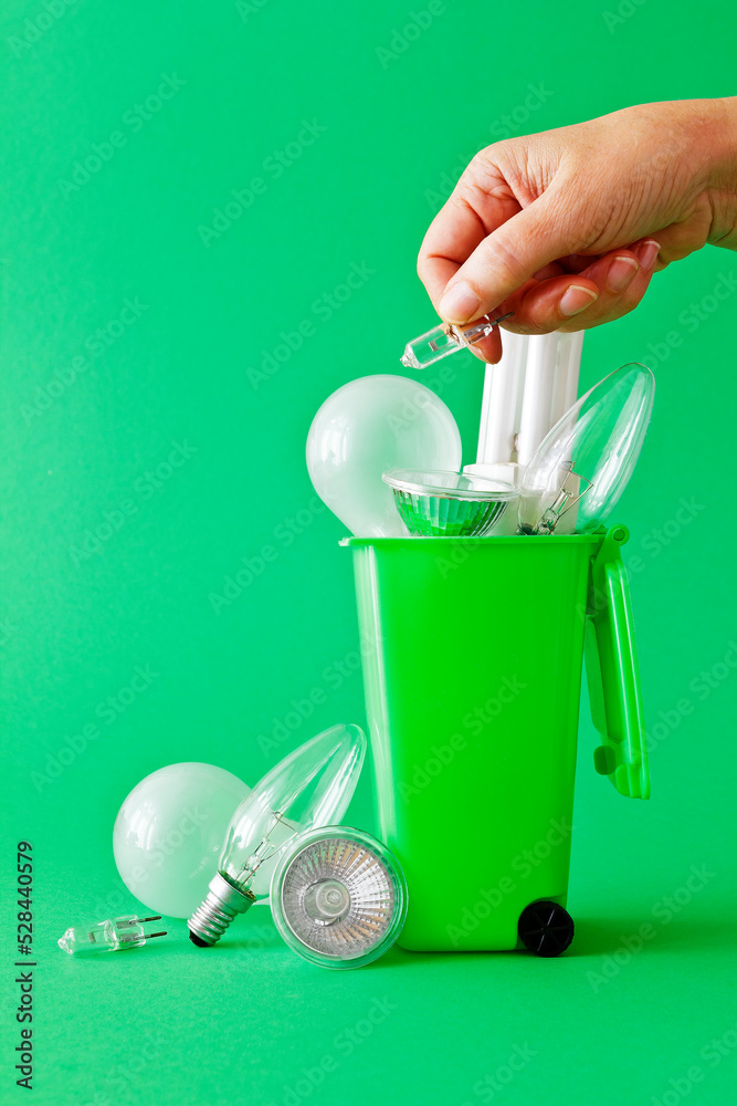 Φωτογραφία Green living concept: diverse old inefficient light bulbs in and around a green recycling bin with a hand throwing another halogen lamp away