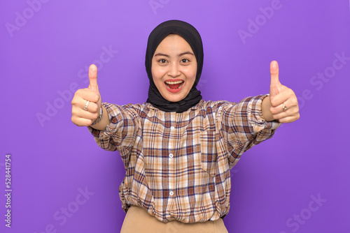 Cheerful young Asian woman in plaid shirt showing thumbs up isolated on purple background