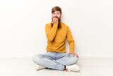 Young caucasian man sitting on the floor isolated on white background relaxed thinking about something looking at a copy space.