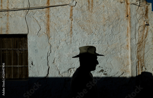 Portrait of adult man in cowboy hat against wall with sunlight and shadow