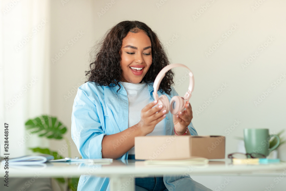 Excited African American Woman Unpacking Box With Headphones At Home Excited African American Woman Unpacking Box With Headphones At Home