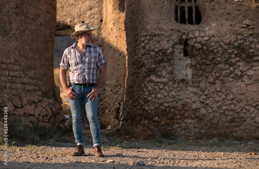 Portrait of adult man in cowboy hat and shirt against abandoned building