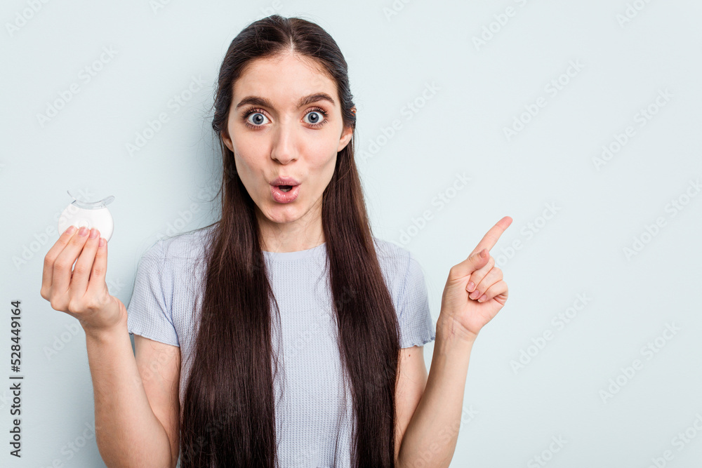 Young caucasian woman holding teeth whitener isolated on blue background pointing to the side Young caucasian woman holding teeth whitener isolated on blue background pointing to the side