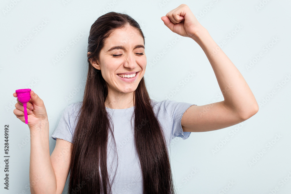 Young caucasian woman holding a sanitary napkin isolated on blue background raising fist after a victory, winner concept. Young caucasian woman holding a sanitary napkin isolated on blue background raising fist after a victory, winner concept.