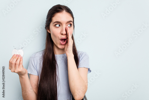 Young caucasian woman holding teeth whitener isolated on blue background is saying a secret hot braking news and looking aside