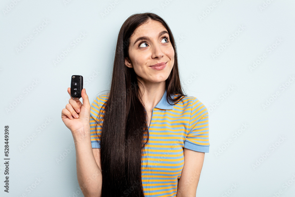 Young caucasian woman holding car keys isolated on blue background dreaming of achieving goals and purposes Young caucasian woman holding car keys isolated on blue background dreaming of achieving goals and purposes