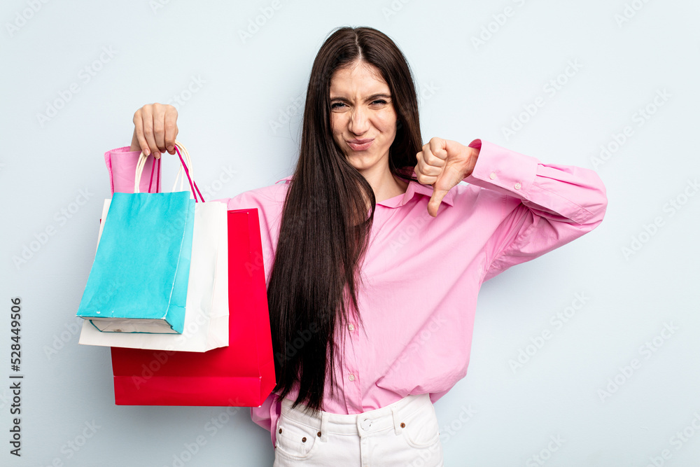 Young caucasian woman going to buy some clothes isolated on blue background showing a dislike gesture, thumbs down. Disagreement concept. Young caucasian woman going to buy some clothes isolated on blue background showing a dislike gesture, thumbs down. Disagreement concept.