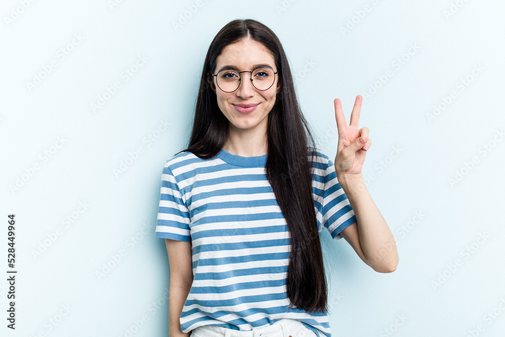 Young caucasian woman isolated on blue background joyful and carefree showing a peace symbol with fingers.
