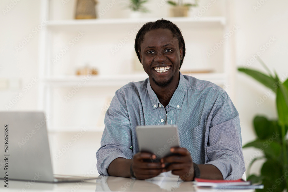 Happy Black Guy Using Digital Tablet While Sitting At Desk At Home Happy Black Guy Using Digital Tablet While Sitting At Desk At Home
