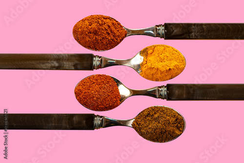 A selection of cayenne pepper tumeric chilli curry powder spices used in Indian cooking on a coulerful pink background photo