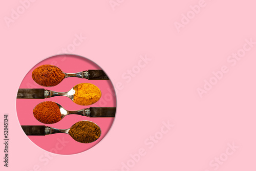 A selection of cayenne pepper tumeric chilli curry powder spices used in Indian cooking on a coulerful light coral pink background photo