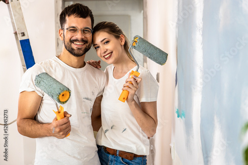 Portrait of young couple painting wall in their home. photo