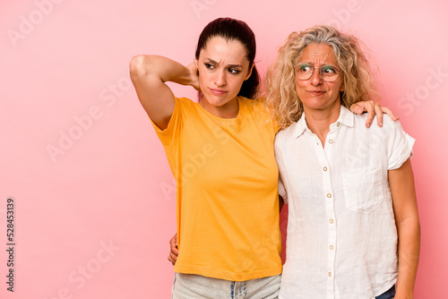 Caucasian mom and daughter isolated on pink background touching back of head, thinking and making a choice.