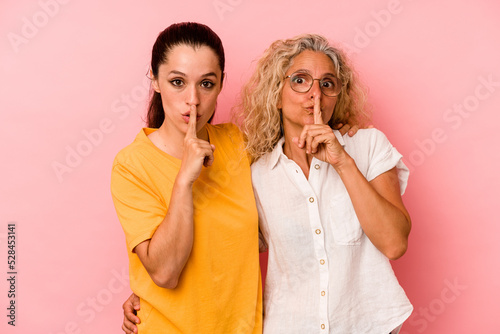 Caucasian mom and daughter isolated on pink background keeping a secret or asking for silence.