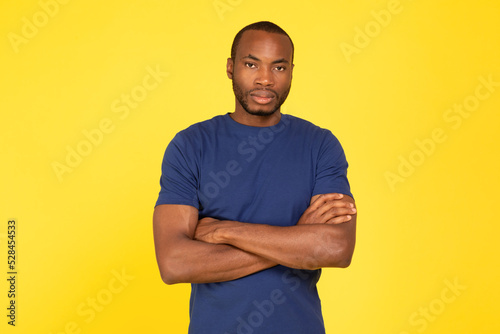 Serious African American Guy Crossing Hands Posing Over Yellow Background