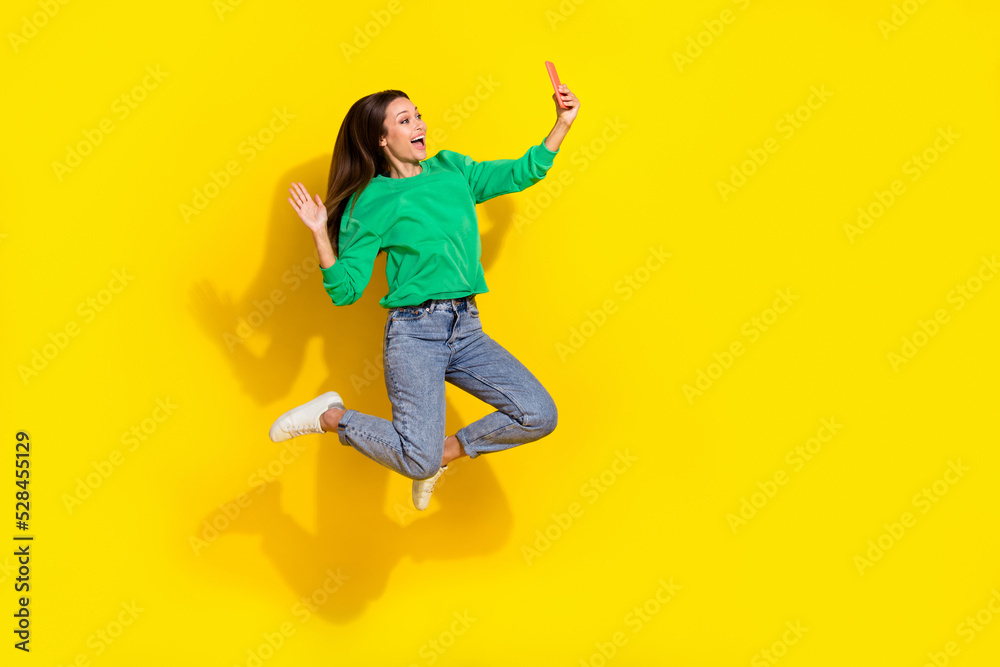 Full body photo of carefree lady jump hold telephone make selfie arm palm waving isolated on yellow color background