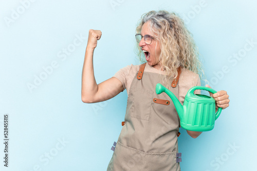 Middle age gardener woman holding a watering can isolated on white background raising fist after a victory, winner concept.