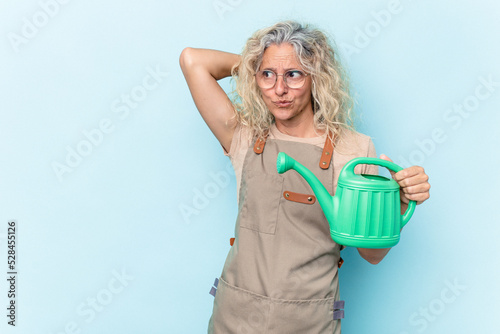 Middle age gardener woman holding a watering can isolated on white background touching back of head, thinking and making a choice.
