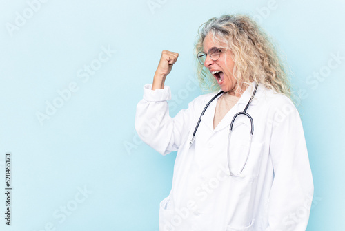 Middle age caucasian woman isolated on blue background raising fist after a victory, winner concept.