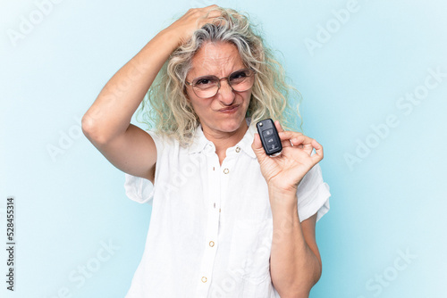 Middle age caucasian woman holding a car keys isolated on blue background being shocked, she has remembered important meeting.