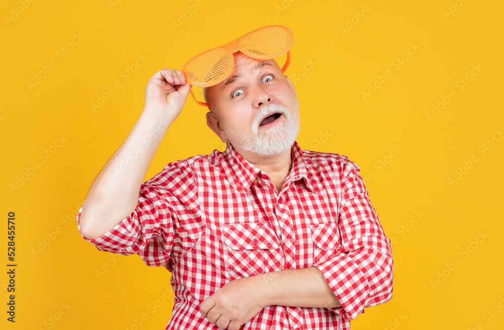 amazed old man in checkered shirt with party glasses on yellow background