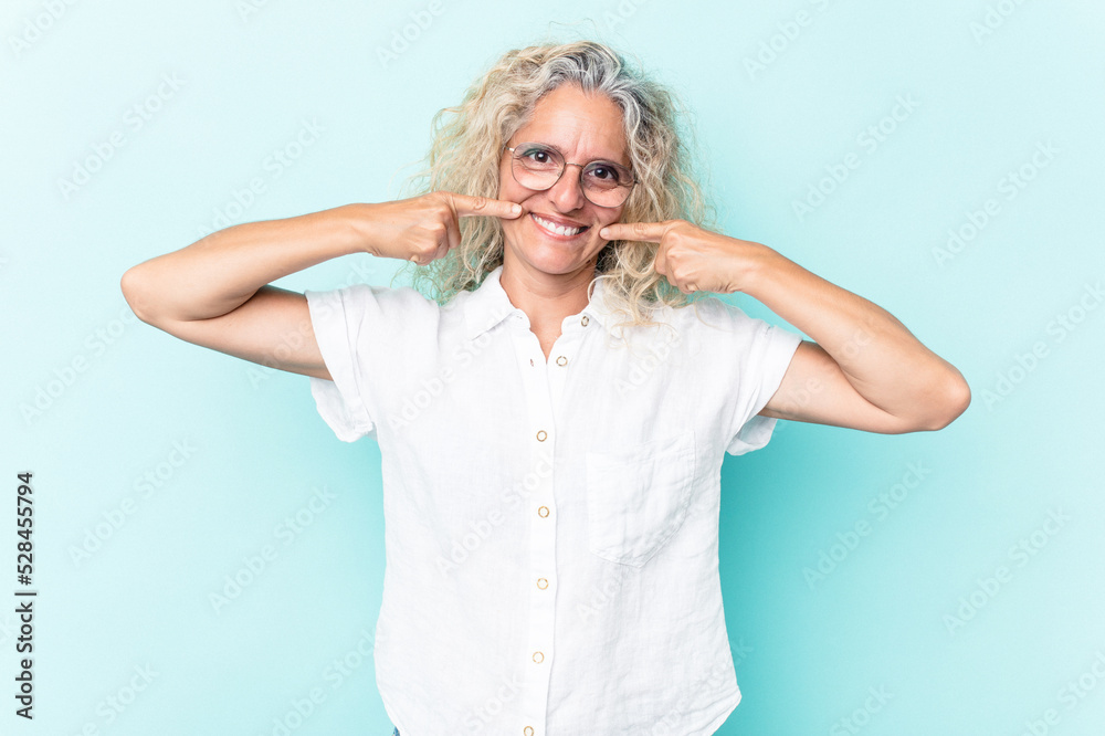 Middle age caucasian woman isolated on blue background smiles, pointing fingers at mouth. Middle age caucasian woman isolated on blue background smiles, pointing fingers at mouth.