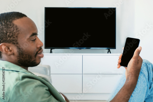 Fotografie Black man watching television with blank screen and using smart TV remote contro