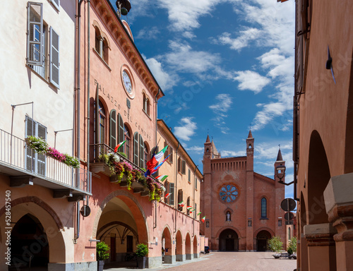 Alba, Langhe, Piedmont, Italy - August 16, 2022: the Town Hall with flowered balconies and medieval arcades in via Cavour, in the background Cathedral of San Lorenzo in Piazza Duomo