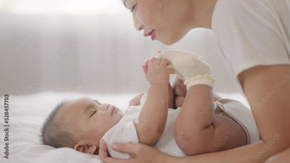 young Asian mother is playing with her newborn baby on the white bed in a home in a morning.Concept of newborn,baby,parenthood,motherhood,childhood,New life,maternity,love,new family member young Asian mother is playing with her newborn baby on the white bed in a home in a morning.Concept of newborn,baby,parenthood,motherhood,childhood,New life,maternity,love,new family member