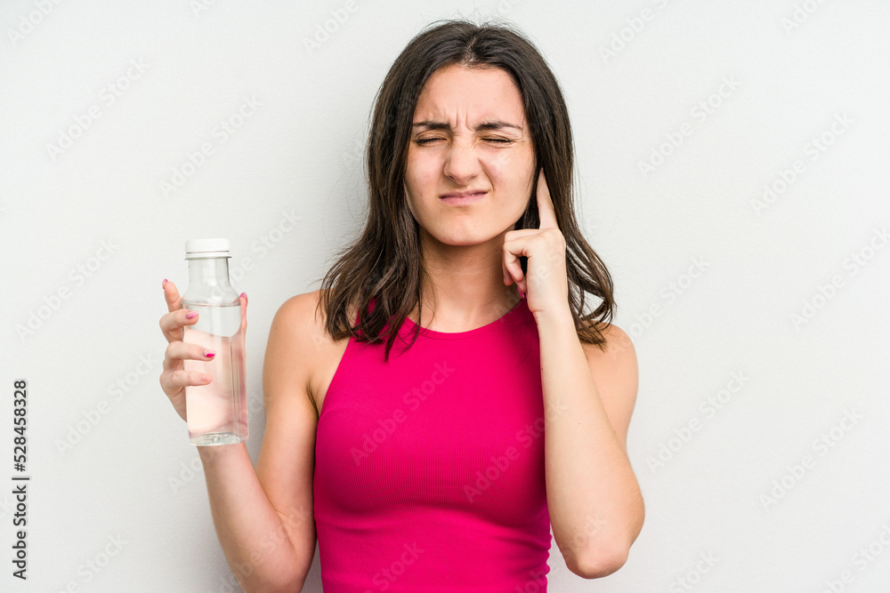 Young caucasian woman holding a bottle of water isolated on white background covering ears with hands. Young caucasian woman holding a bottle of water isolated on white background covering ears with hands.