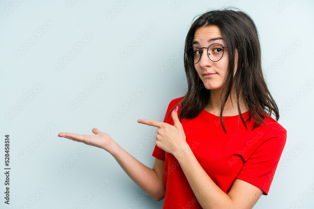 Young caucasian woman isolated on blue background excited holding a copy space on palm. Young caucasian woman isolated on blue background excited holding a copy space on palm.