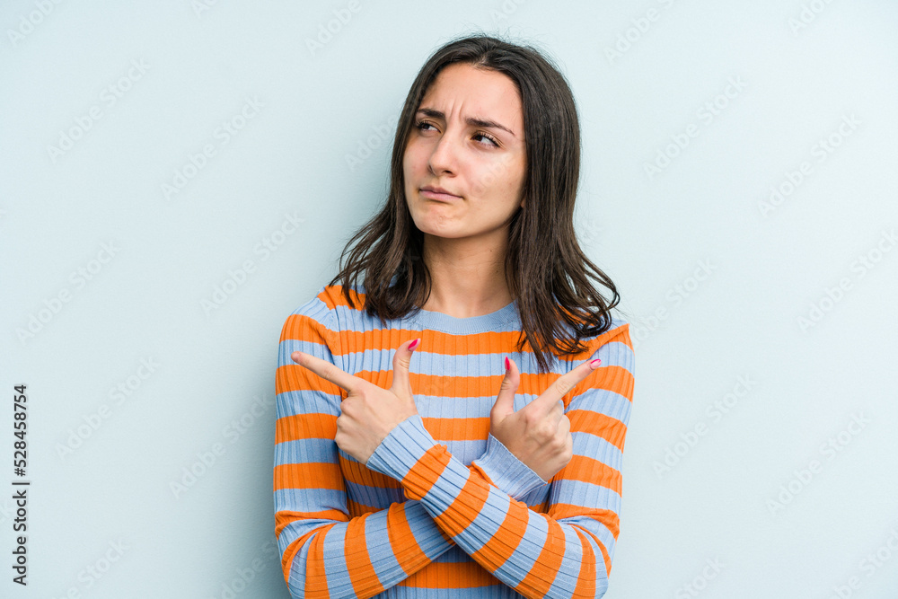 Young caucasian woman isolated on blue background points sideways, is trying to choose between two options. Young caucasian woman isolated on blue background points sideways, is trying to choose between two options.