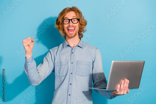 Photo of pretty successful man wear denim shirt spectacles communicating modern gadget rising fist isolated blue color background