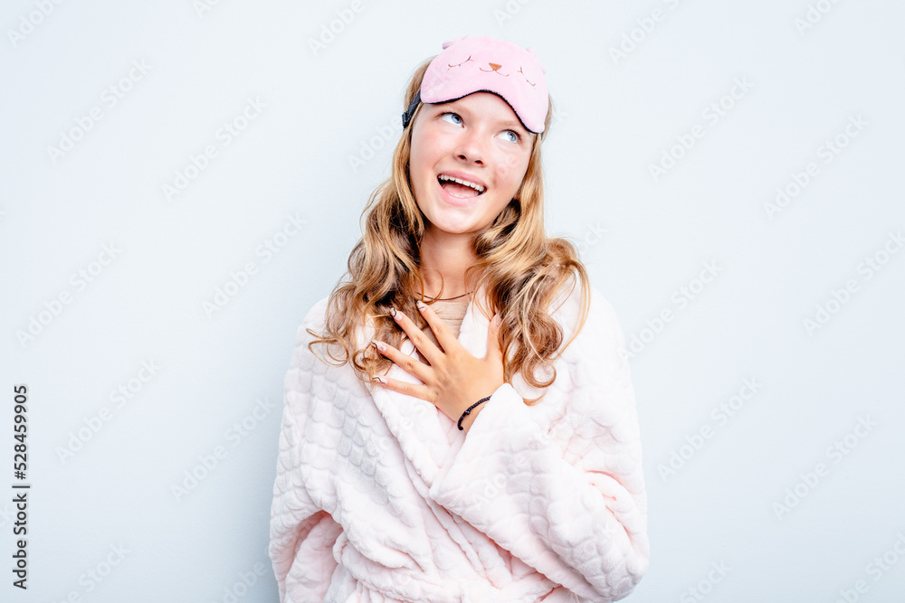 Caucasian teen girl wearing a pajama isolated on blue background laughs out loudly keeping hand on chest. Caucasian teen girl wearing a pajama isolated on blue background laughs out loudly keeping hand on chest.