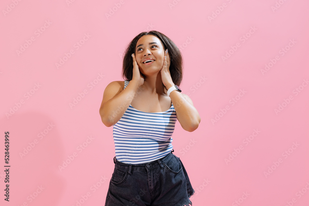 Surprise, delight. Beautiful african girl wearing summer striped tank top and shorts looking at camera isolated on pink background.