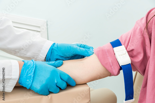 Cropped hands of nurse in blue gloves prepare patient's right hand for blood sampling procedure.