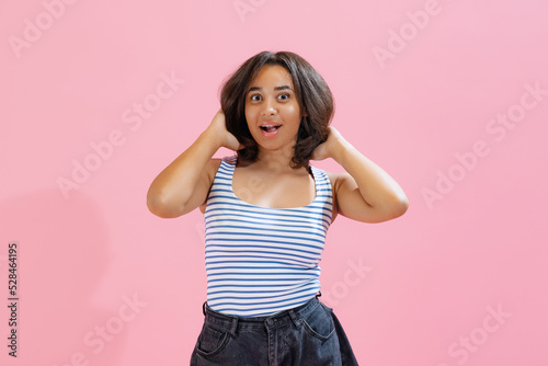 Shocked beautiful african girl wearing summer striped tank top and shorts looking at camera isolated on pink background. Beauty, art, fashion, emotions concept