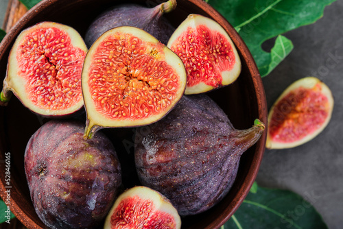 Fresh figs and fig halves on a brown old clay plate. Dark background, close-up top view. Seasonal ripe fruits, mediterranean diet