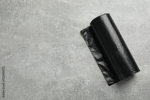 Roll of black garbage bags on grey stone table, top view. Space for text